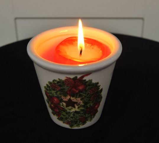 Punainen kynttilä palaa kupissa, jossa on jouluaiheinen koristepainatus.