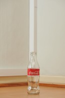 Tyhjä lasinen 0,25 litran Coca-Cola-pullo puunvärisellä lattialla.