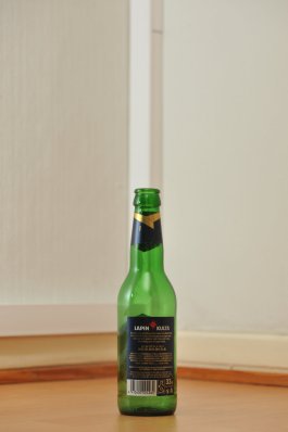Tyhjä Lapin Kulta -oluen vihreä 0,33 litran lasipullo puunvärisellä lattialla.