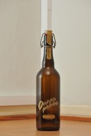 Tyhjä Onnenpekka-oluen 0,75 litran ruskea patenttikorkkipullo puunvärisellä lattialla.