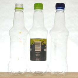 Kolme samanmuotoista muovipulloa, joista keskimmäisessä on etiketti.