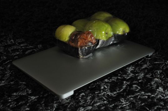 Macbook-kannettavan päällä rasia vihreitä omenoita, joista yksi on pilaantunut.