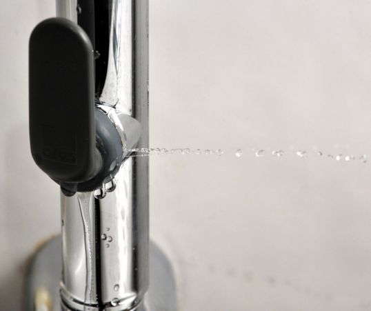 Käsisuihku, jonka liipaisimen kohdalta sinkoutuu vesipisaroita vaakasuoraan ja vuotaa vettä alaspäin.