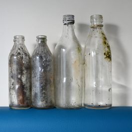 Neljä metsästä löytynyttä likaista ja etiketitöntä lasipulloa.