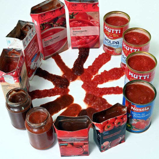 Erilaisia tomaattimurskasäilyketölkkejä ja -purkkeja ja niiden sisältöä valkoisella alustalla.