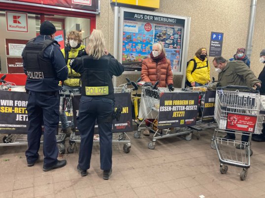 Kaksi poliisia ja ruokaa tutkivia ihmisiä ruokaa ostoskärryistä jakavien ihmisten edessä.